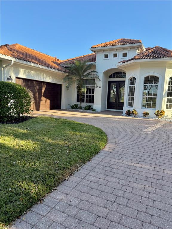 Mediterranean / spanish house with curved driveway, stucco siding, french doors, a tile roof, and a front lawn