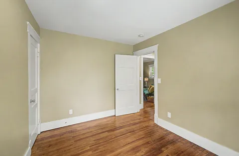 a view of an empty room with wooden floor and closet