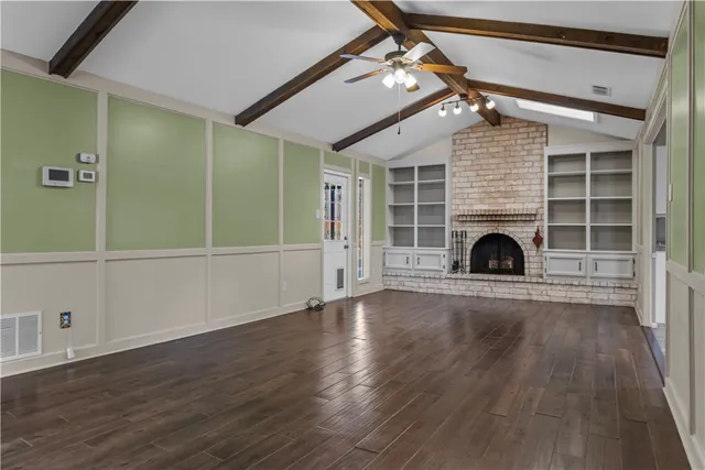 an empty room with wooden floor a fireplace and windows