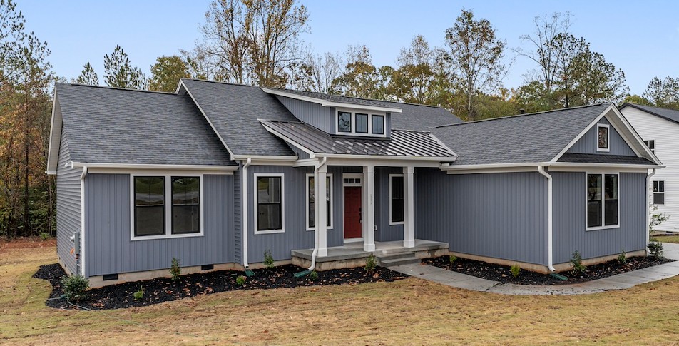 This charming modern home features striking blue siding and a classic gray roof, nestled amidst lush greenery.