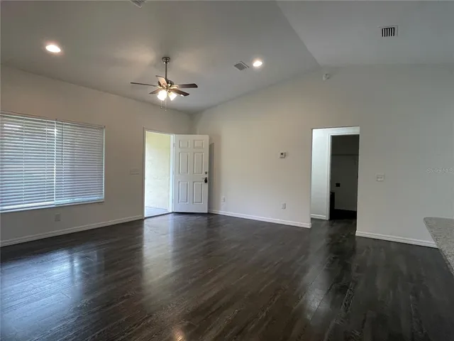 a view of an empty room with wooden floor and a ceiling fan