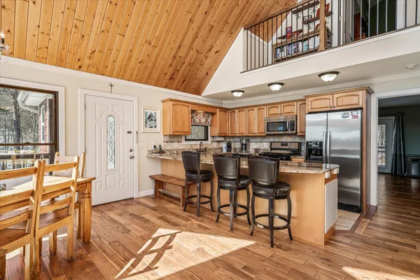 a kitchen with stainless steel appliances kitchen island granite countertop a refrigerator a stove a dining table and chairs with wooden floor