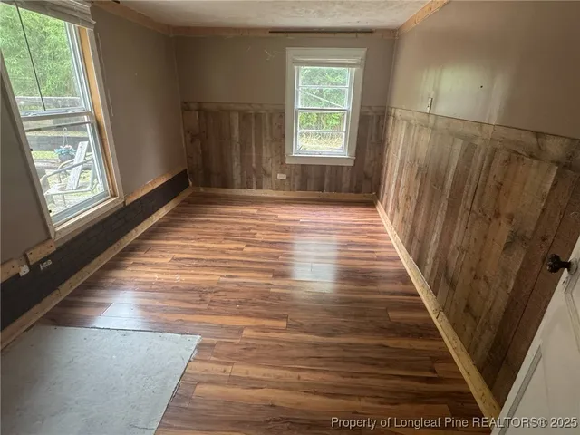 an empty room with wooden floor chandelier fan and windows