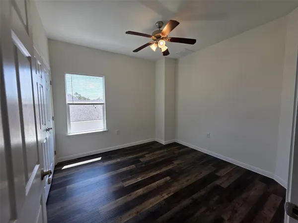 an empty room with wooden floor fan and windows