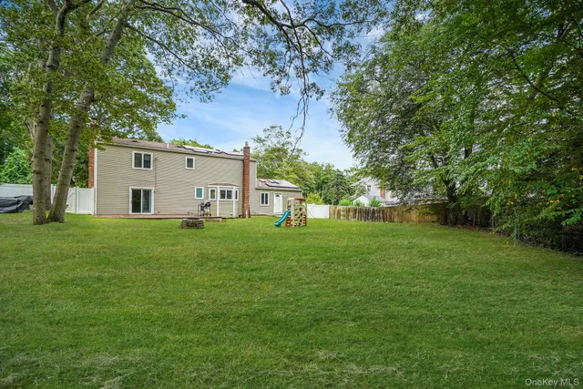 a view of a white house in front of a big yard with large trees