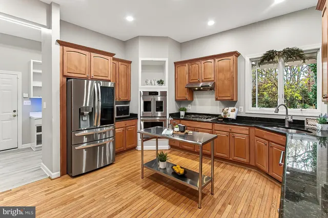 a kitchen with stainless steel appliances granite countertop a refrigerator a stove and a sink with wooden floor