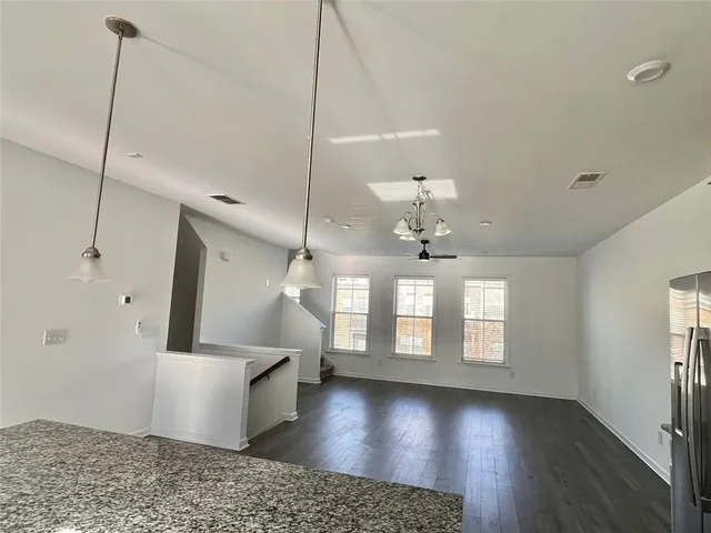 a view of an empty room with wooden floor and a kitchen