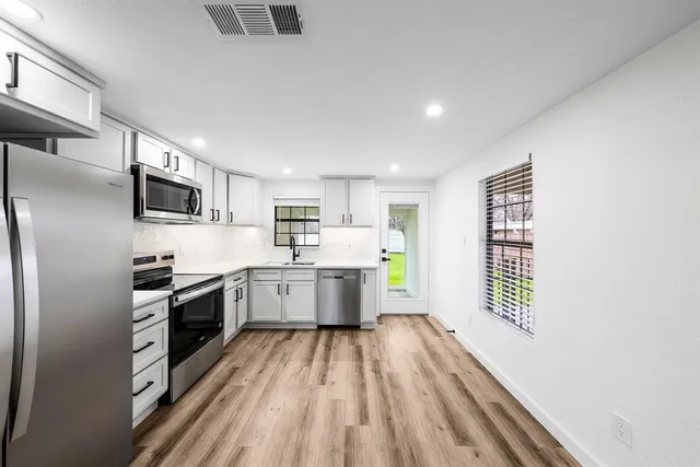 a large kitchen with a center island wooden floor stainless steel appliances and cabinets
