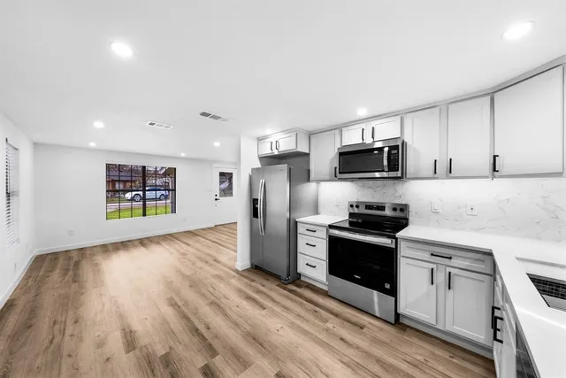 a kitchen with stainless steel appliances granite countertop a stove top oven a sink dishwasher and a refrigerator with wooden floor