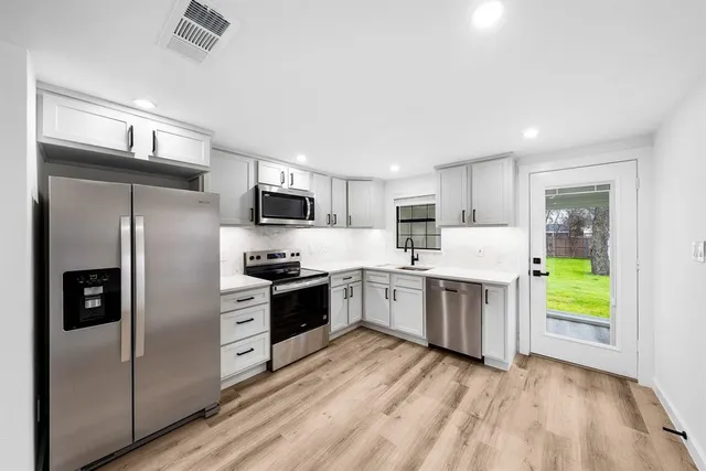 a kitchen with a refrigerator a stove top oven a sink dishwasher and white cabinets with wooden floor