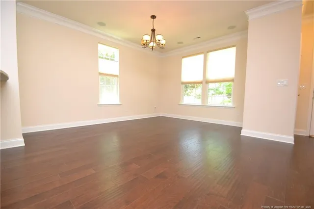 an empty room with wooden floor chandelier and windows