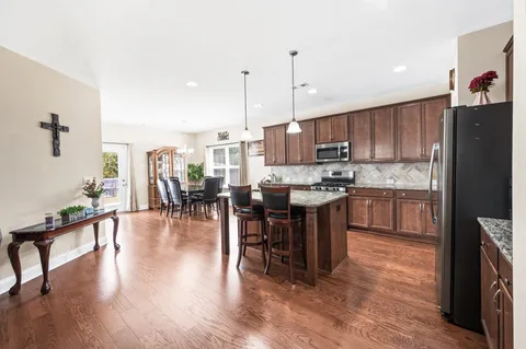 a kitchen with stainless steel appliances granite countertop a refrigerator a stove top oven a sink dishwasher and a dining table with wooden floor