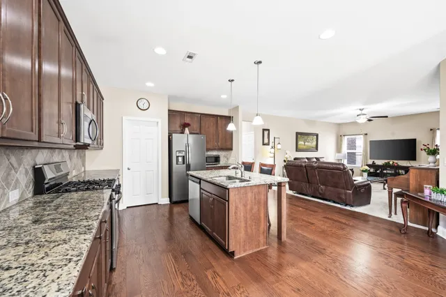 a kitchen with stainless steel appliances granite countertop a stove top oven a sink dishwasher and a refrigerator with wooden floor