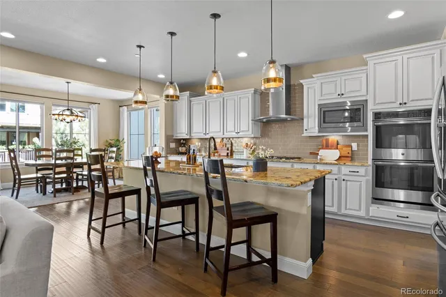 a open kitchen with stainless steel appliances granite countertop a stove a refrigerator a kitchen island a dining table and chairs with wooden floor