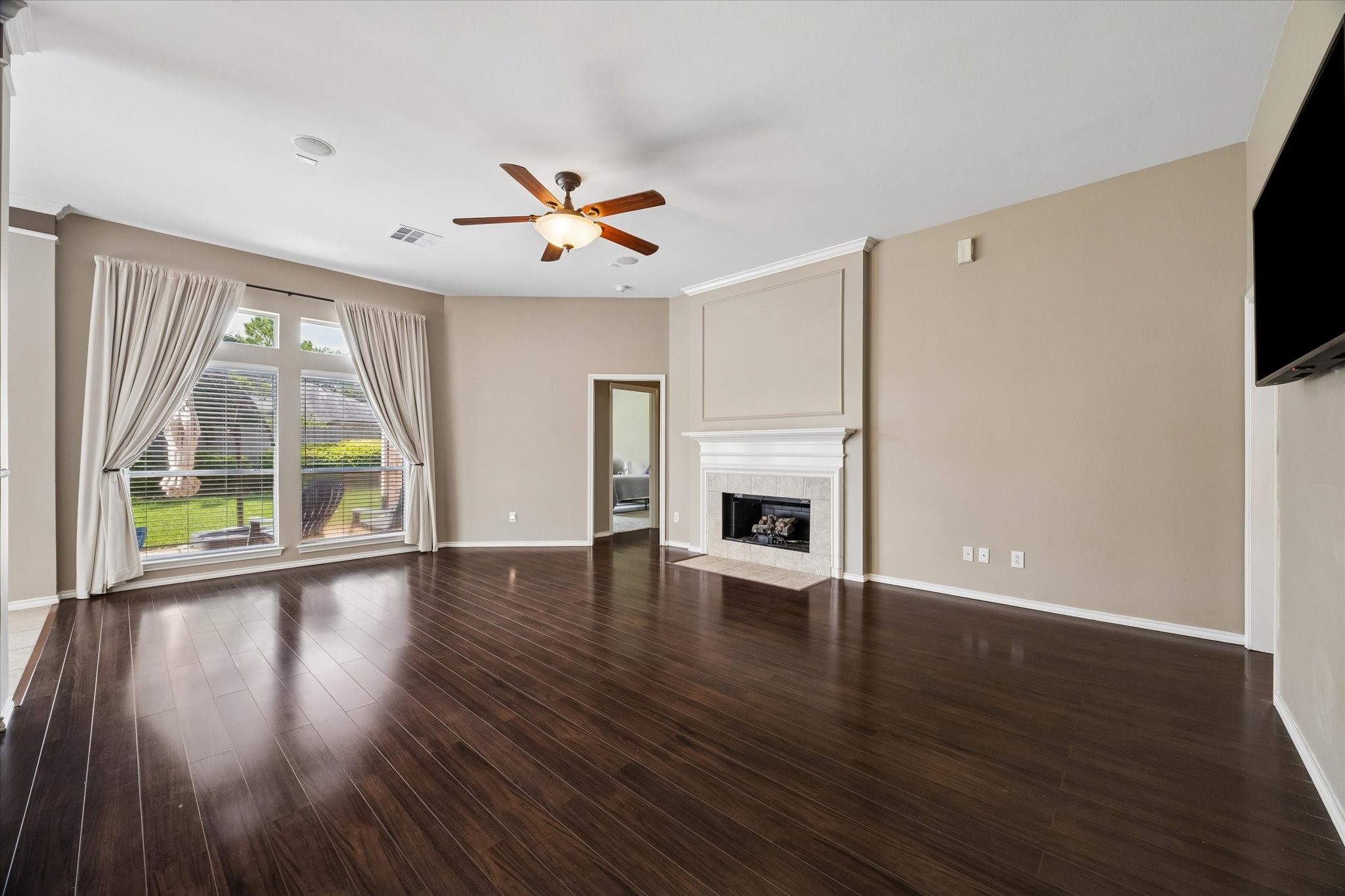 3118 Valley Court Manvel, TX 77578 - Photo 27 of 38 This spacious living room features dark hardwood floors, a cozy fireplace, and large windows with elegant drapes that bring in plenty of natural light. The neutral walls and ceiling fan add a touch of modern comfort.