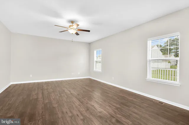 an empty room with wooden floor ceiling fan and windows