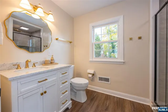 a bathroom with a granite countertop toilet a sink a mirror and a window