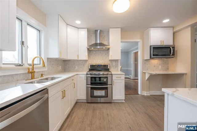 a kitchen with kitchen island granite countertop a stove top oven a sink dishwasher and white cabinets with wooden floor