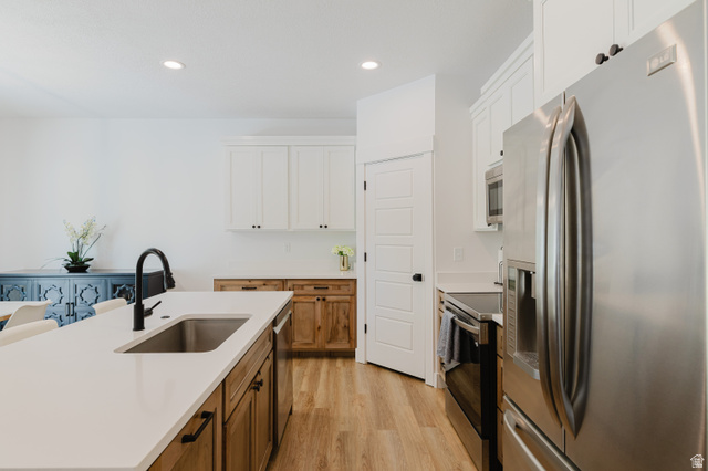 287 East 1000 North Logan, UT 84321 - Photo 12 of 41 Kitchen featuring an island with an undermount sink and matte black faucet, white upper cabinetry, wood-finish lower cabinetry, and stainless steel appliances