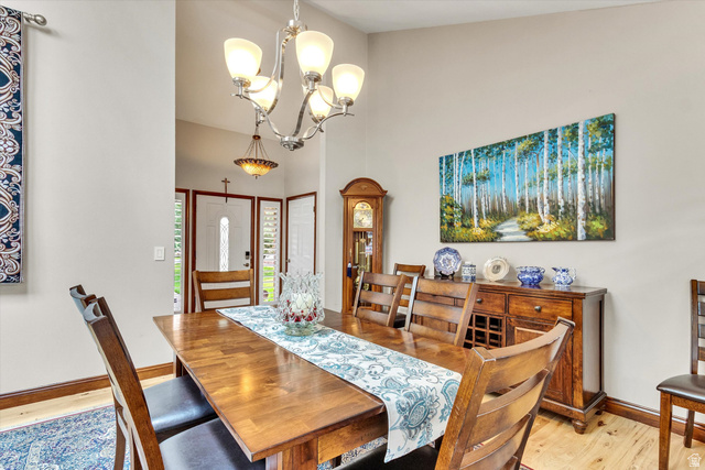 2863 Fallentine Road Sandy, UT 84093 - Photo 21 of 48 Dining area with a wood-finish table, featuring a multi-light chandelier, light-toned walls, wood-finish flooring, and a detailed front entry door with transom