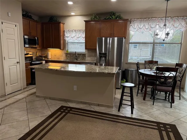 a room with stainless steel appliances kitchen island granite countertop a sink refrigerator and cabinets