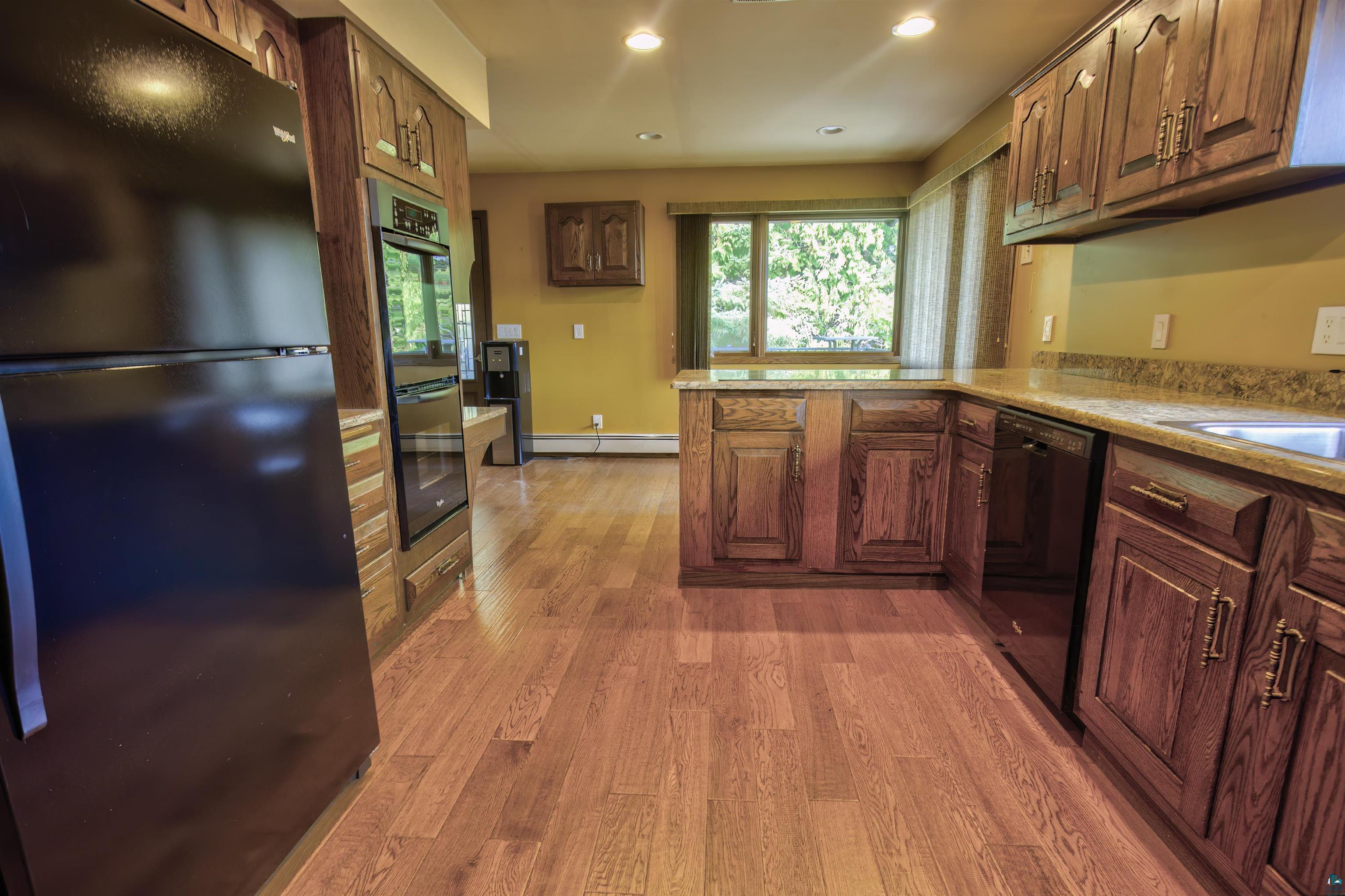 1933 West Shagawa Road Ely, MN 55731 - Photo 13 of 46 Kitchen with a baseboard heating unit, kitchen peninsula, wood-type flooring, sink, and black appliances