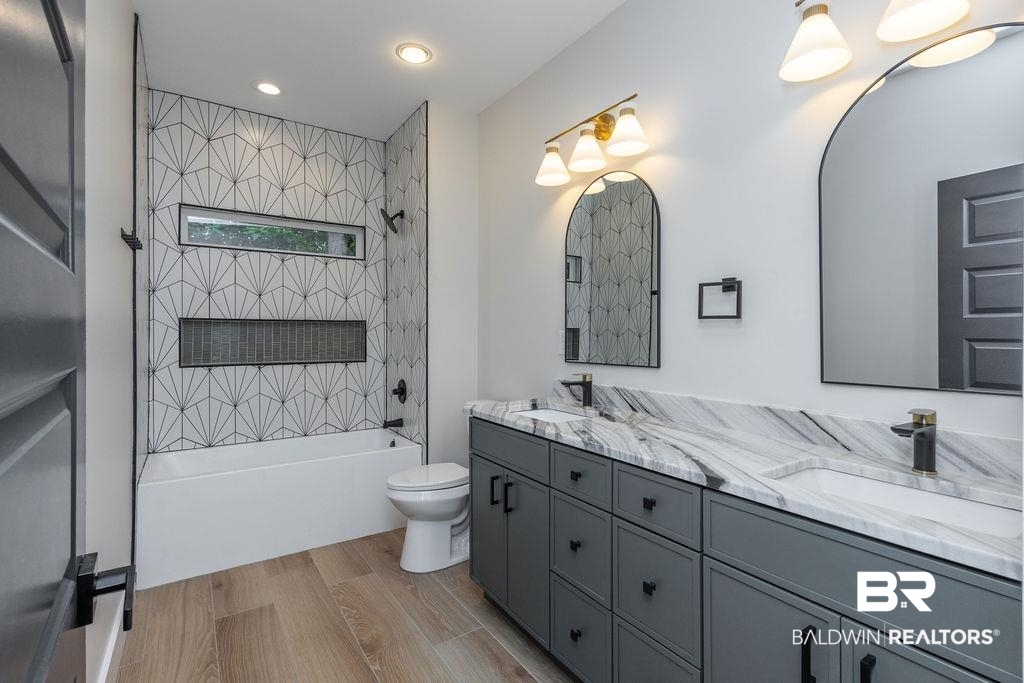 13066 Gopher Court Elberta, AL 36530 - Photo 20 of 38 Contemporary bathroom featuring a dual vanity with a patterned stone countertop, gray cabinetry, and two arched mirrors