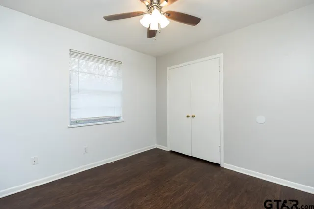 an empty room with wooden floor chandelier fan and windows
