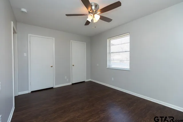 an empty room with wooden floor ceiling fan and windows