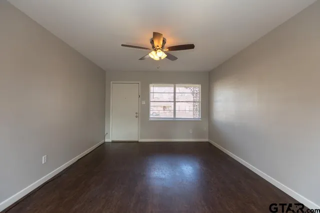 an empty room with wooden floor ceiling fan and windows