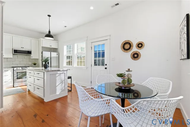 a kitchen with stainless steel appliances granite countertop a stove a microwave a dining table and chairs with wooden floor