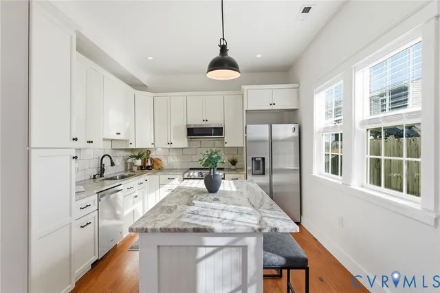 a kitchen with stainless steel appliances granite countertop a stove top oven a refrigerator a sink and white cabinets with wooden floor