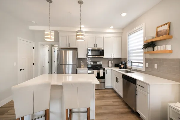 a kitchen with stainless steel appliances granite countertop a refrigerator a sink dishwasher a stove top oven a kitchen island and chairs with wooden floor