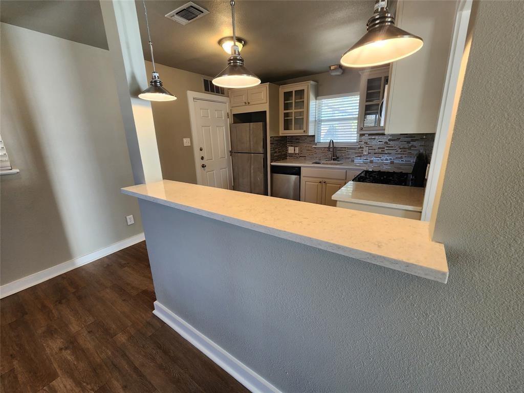 2708 St Edwards Circle, Unit A Austin, TX 78704 - Photo 4 of 13 Kitchen featuring glass insert cabinets, light stone countertops, backsplash, freestanding refrigerator, and dark wood-style floors