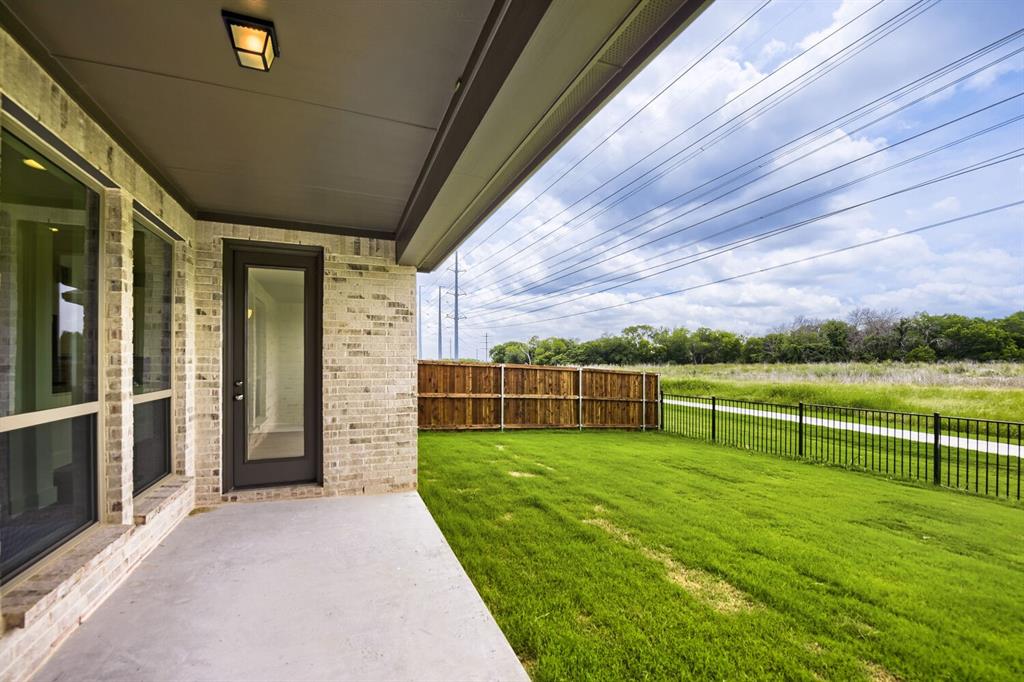 11465 Wulstone Road Fort Worth, TX 76052 - Photo 26 of 27 Covered patio with light-toned brick facade, black framed full-light door, and large windows
