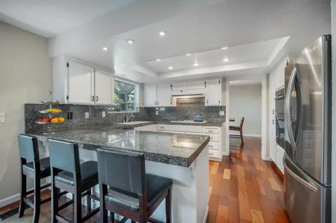 a kitchen with stainless steel appliances granite countertop a stove top oven a refrigerator a sink and a dining table with wooden floor