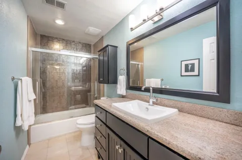 a bathroom with a granite countertop sink a toilet a mirror and shower
