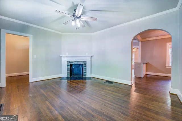 an empty room with wooden floor a ceiling fan a fireplace and windows