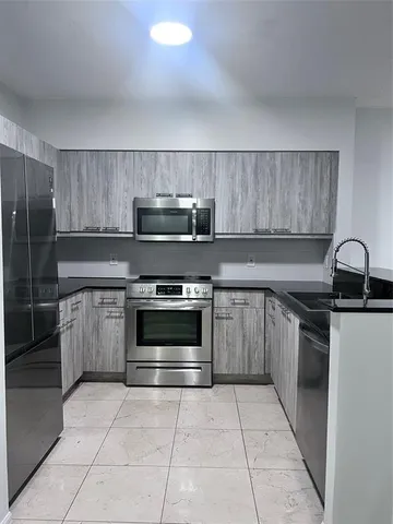 a kitchen with granite countertop a stove a sink and a refrigerator with wooden cabinets