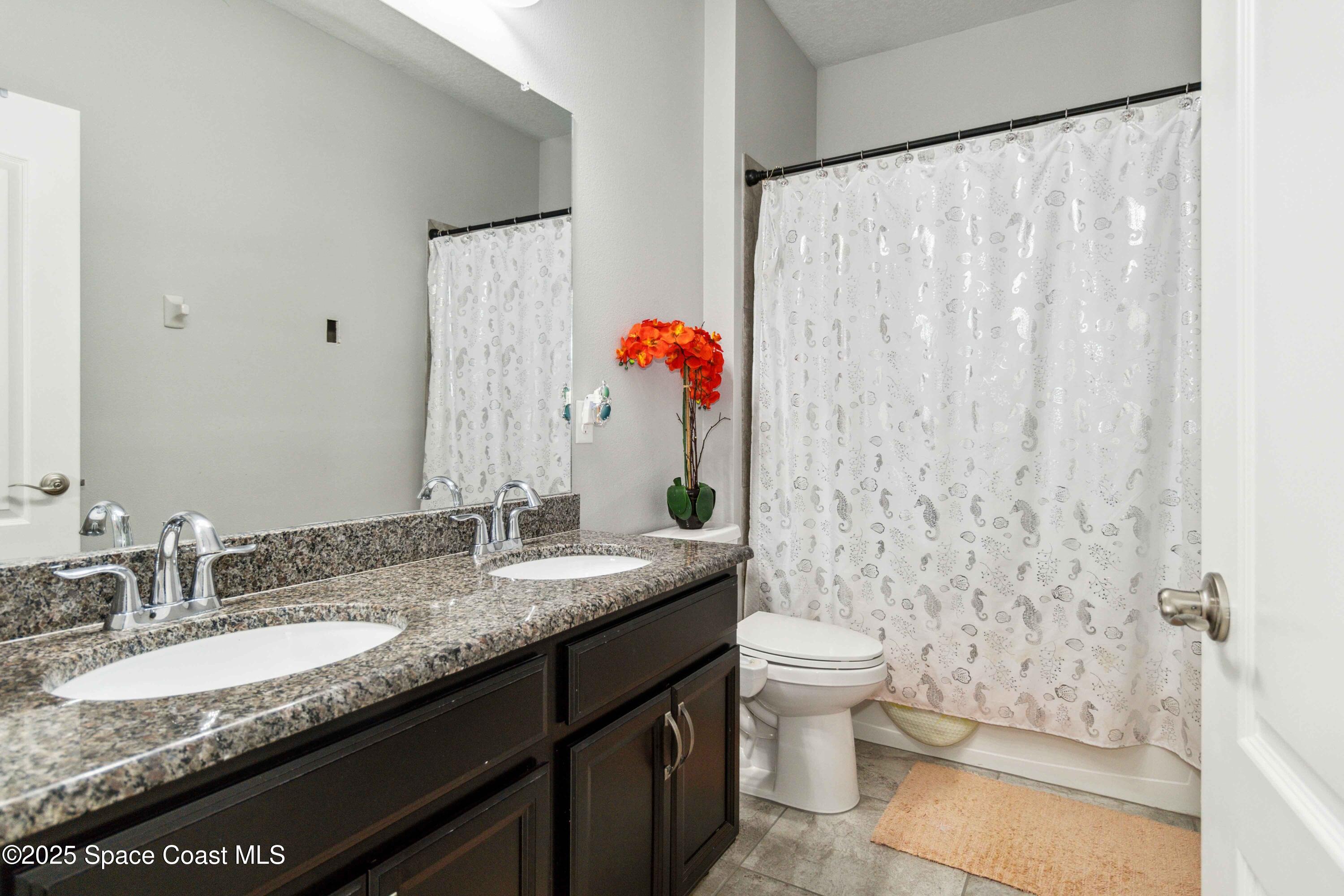 7565 Millbrook Avenue Melbourne, FL 32940 - Photo 22 of 47 a bathroom with a granite countertop sink a toilet and a shower curtain