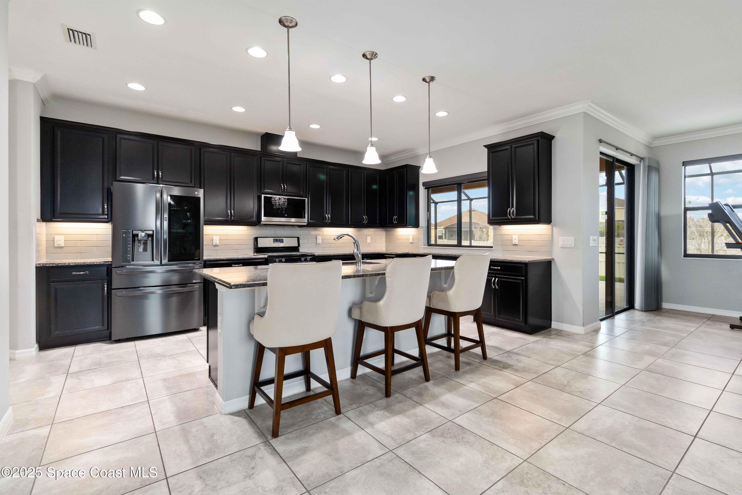 7565 Millbrook Avenue Melbourne, FL 32940 - Photo 7 of 47 a kitchen with stainless steel appliances kitchen island granite countertop a refrigerator a stove a sink a dining table and chairs
