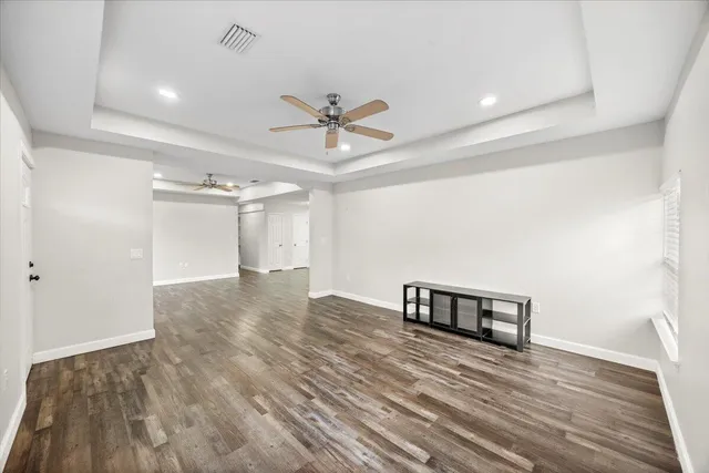 a view of an empty room with chandelier fan and wooden floor