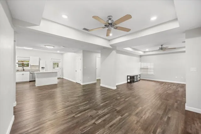 a view of an empty room and kitchen view with wooden floor