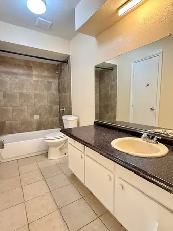 a bathroom with a granite countertop sink a toilet a mirror and bathtub