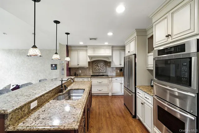 a large kitchen with kitchen island granite countertop a stove a sink a refrigerator and a wooden floor