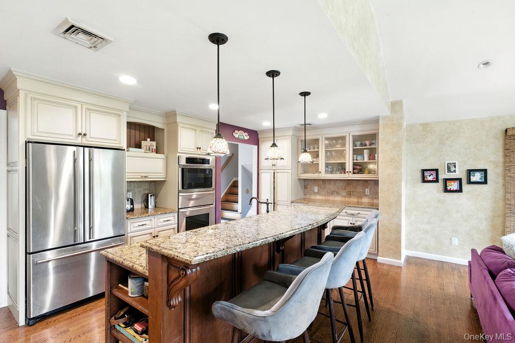 21 Macarthur Avenue Plainview, NY 11803 - Photo 10 of 26 a kitchen with kitchen island a refrigerator a stove a dining table and chairs with wooden floor