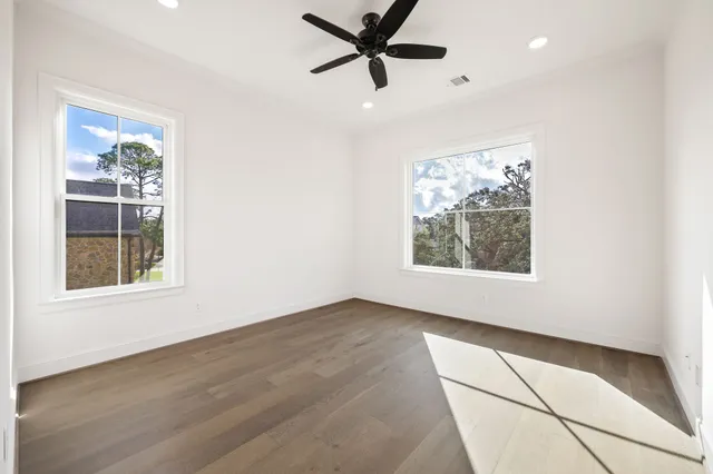 an empty room with wooden floor a ceiling fan and windows