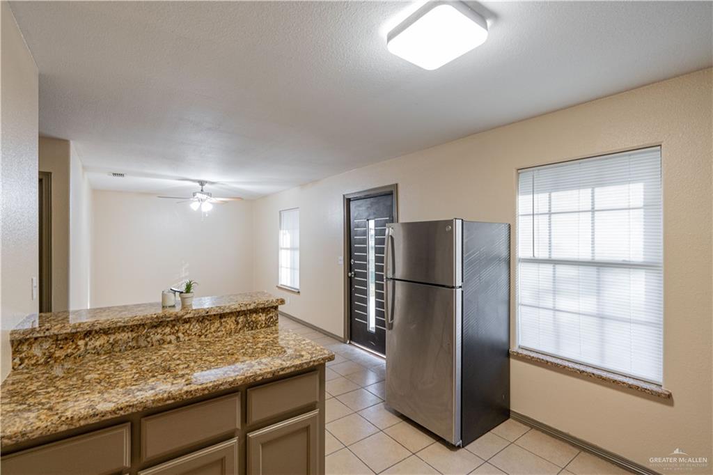 17002 Queen Palm Drive, Unit C Penitas, TX 78576 - Photo 4 of 10 Kitchen with freestanding refrigerator, light stone counters, light tile patterned floors, a ceiling fan, and a textured ceiling