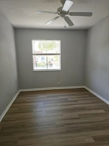 an empty room with wooden floor windows and fan
