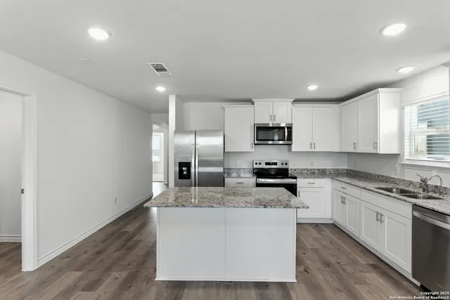 a large kitchen with stainless steel appliances granite countertop a stove a sink dishwasher and a refrigerator with wooden floor